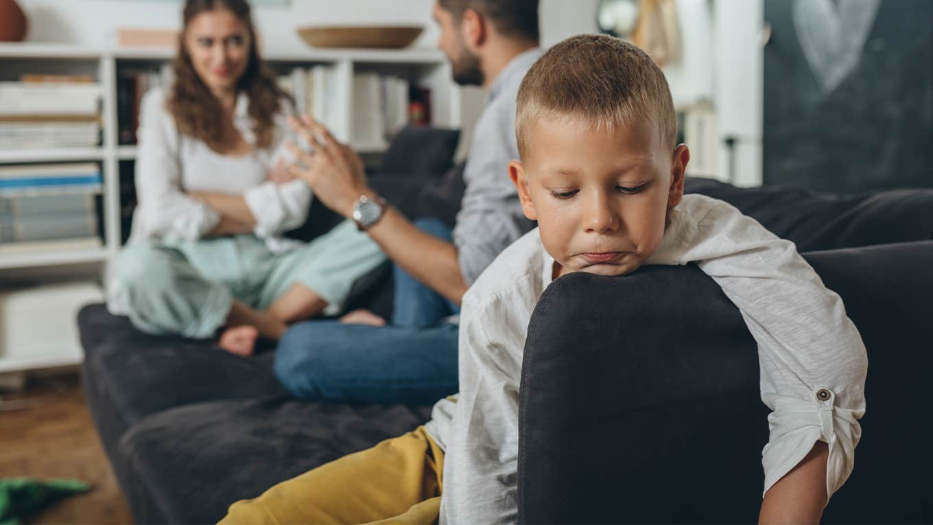 sad little boy with parents arguing behind him