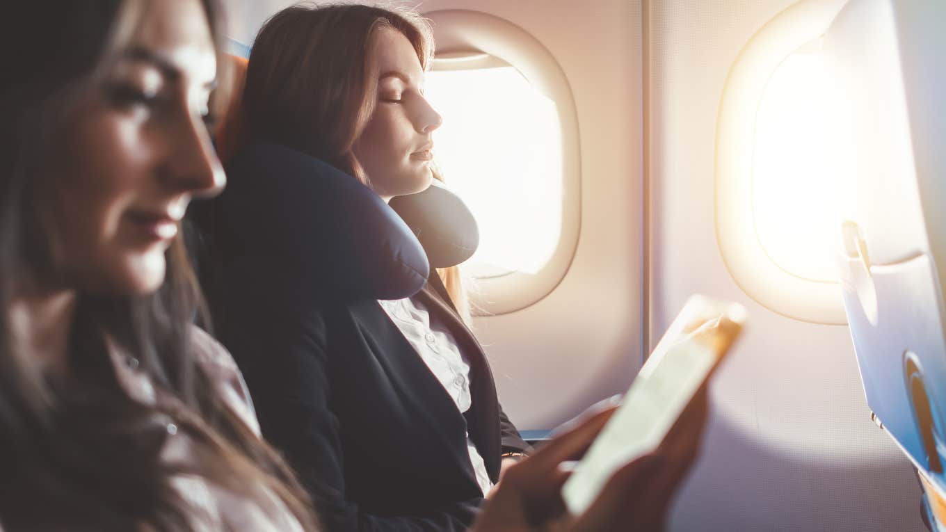 woman sleeping on flight sitting beside window while woman sitting beside her reads e-book