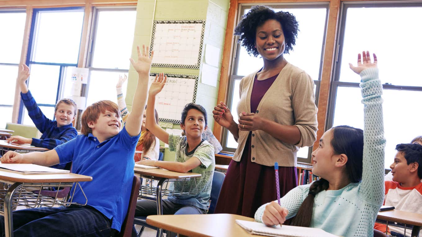 students raising their hand in classroom while teacher walks around
