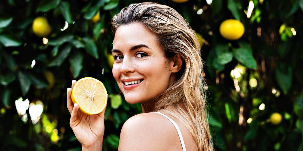 smiling blonde woman holding a lemon in a lemon grove