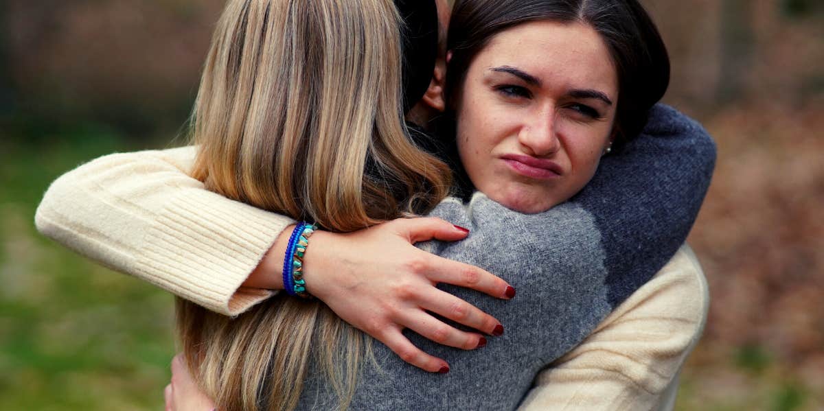 woman hugging woman she doesn't like because she's forcing a friendship