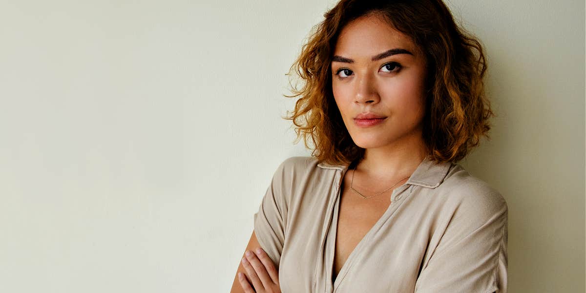 thoughtful woman with arms crossed, leaning against a wall