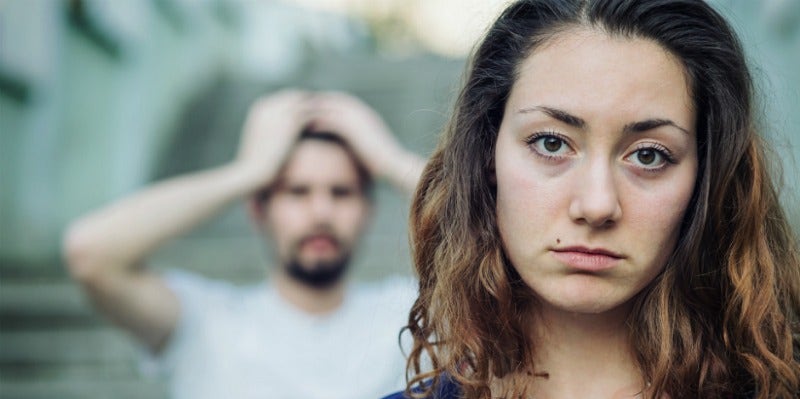 man looking exasperated behind woman looking solemn