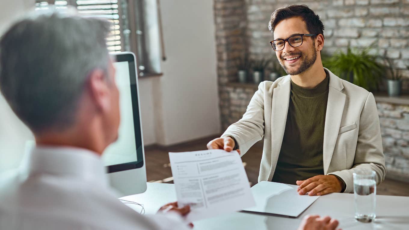 Young happy man applying for job and giving his CV to a manager during the interview in the office.