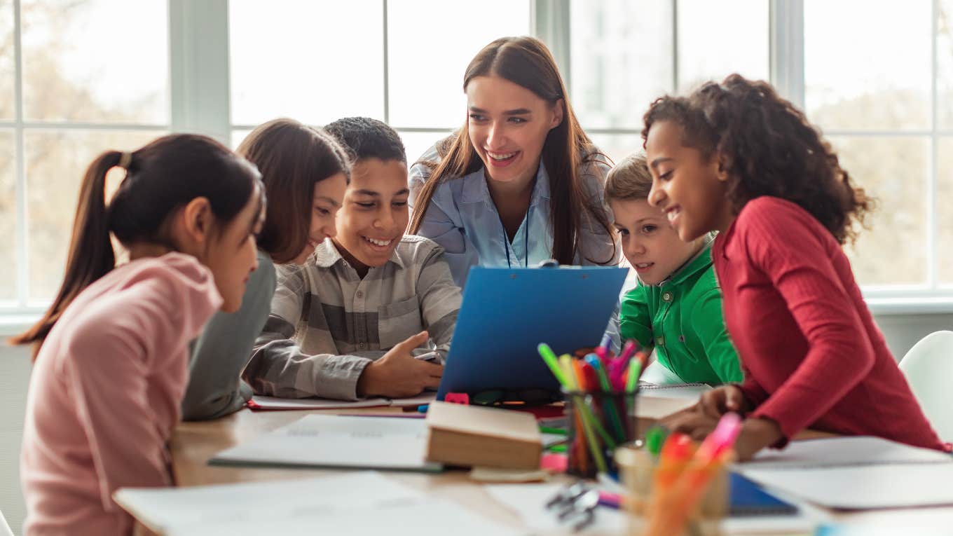 teacher with group of students working on schoolwork sitting around table in classroom