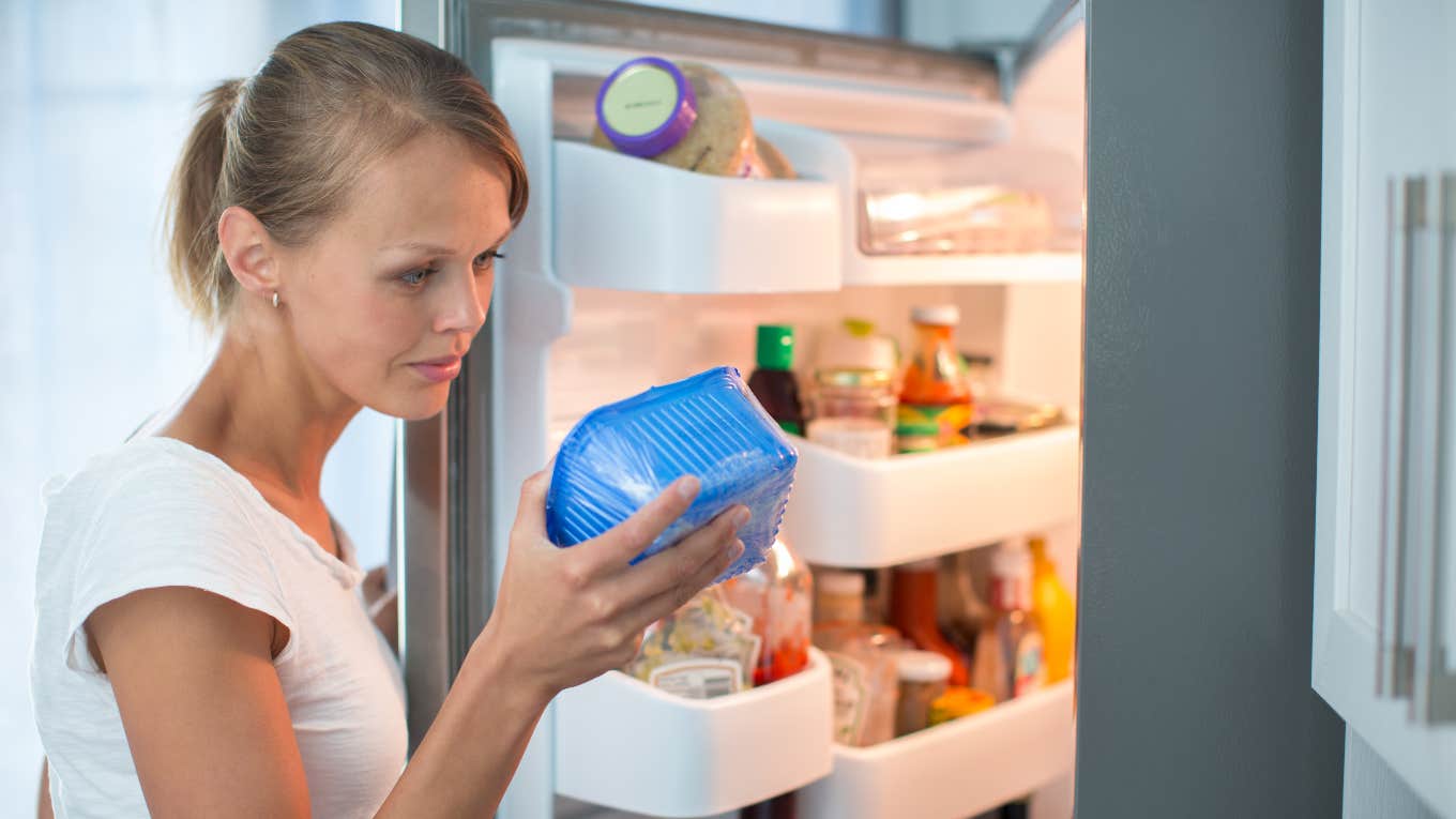 Women looking at produce in her refrigerator. 