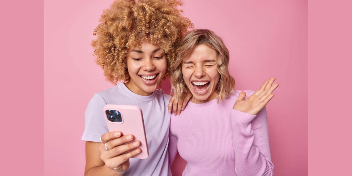 Overjoyed young women laugh happily holding mobile phone 