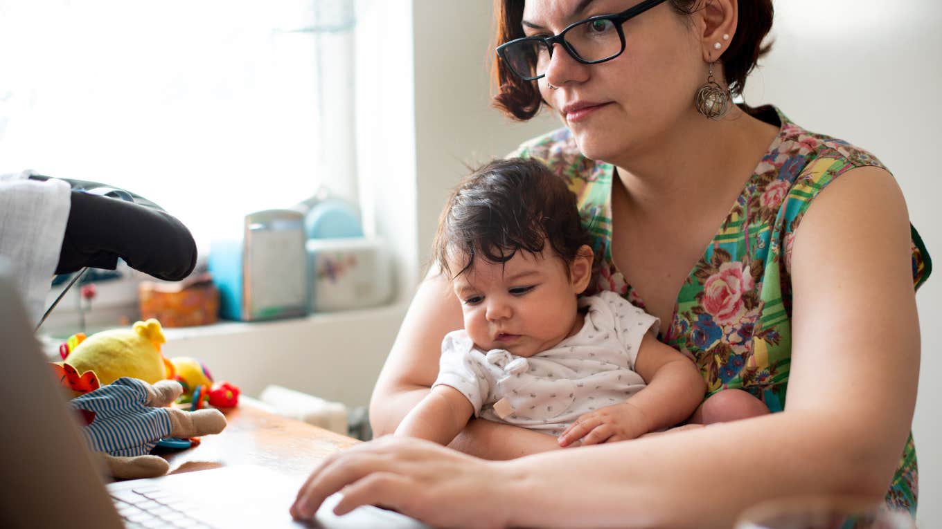 mom holding baby while working on laptop