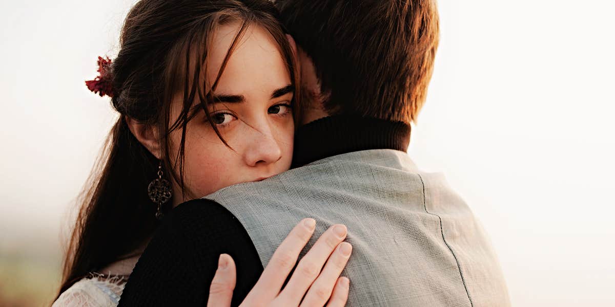 woman looks into camera with sad eyes, hugging a man