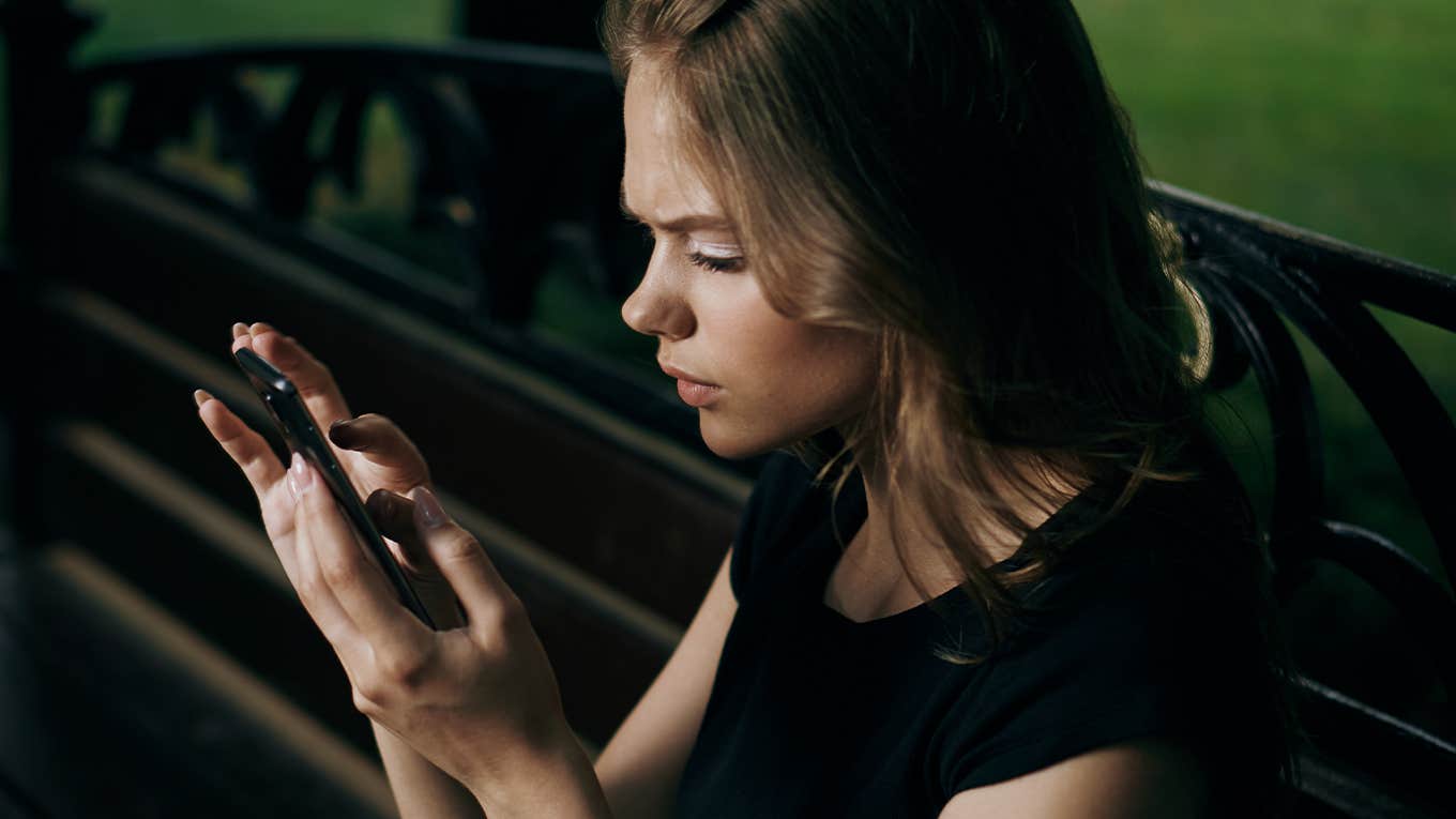 Young beautiful woman is sitting in the phone on a park bench in summer.