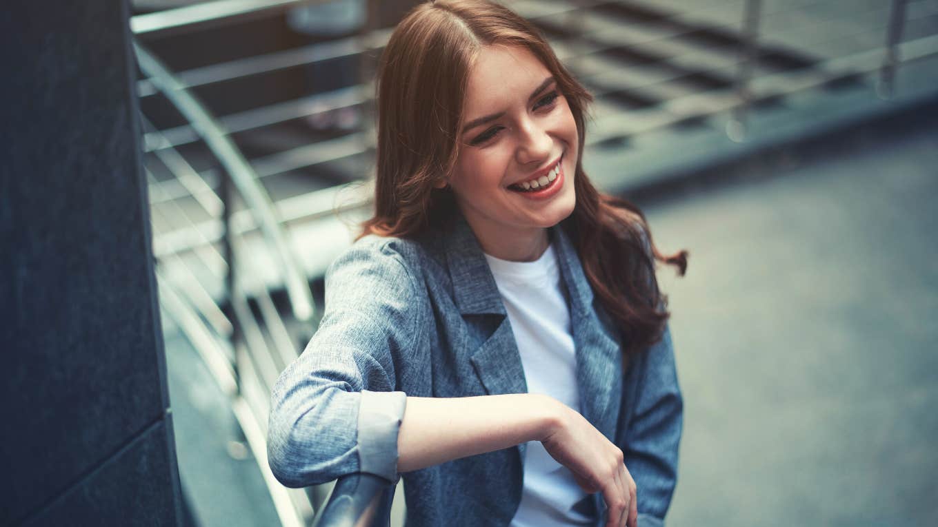 Waist up portrait of laughing attractive young woman standing near the stairs