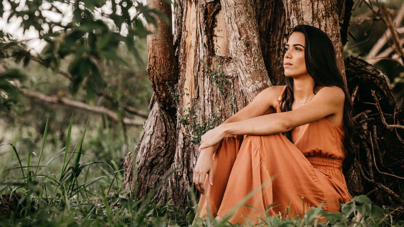 woman thinking in orange dress sitting against tree