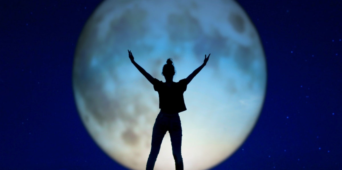woman standing in front of full moon with arms open