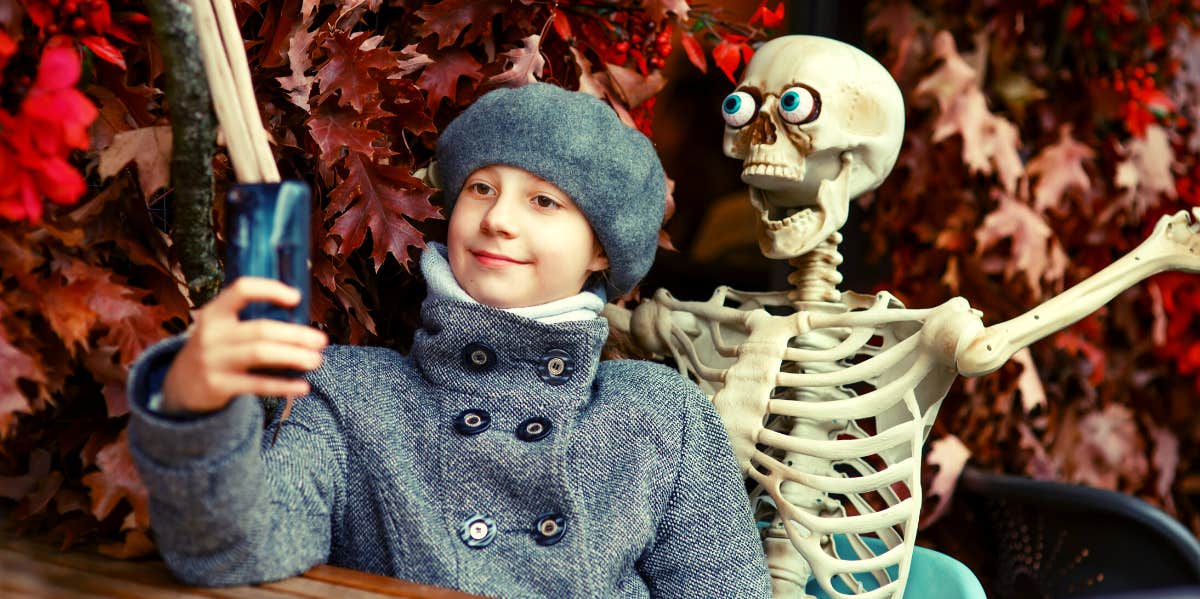 Best Halloween Instagram Captions For Cute, Funny & Spooky Pics kid with skeleton decoration taking picture to post on Instagram
