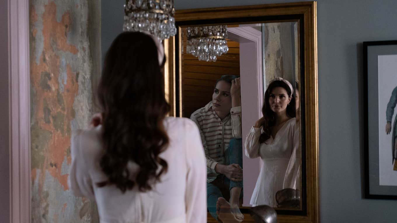 Woman standing in front of a mirror dressed up, her reflection showing her in clothes that do not make her feel good, sitting unhappy