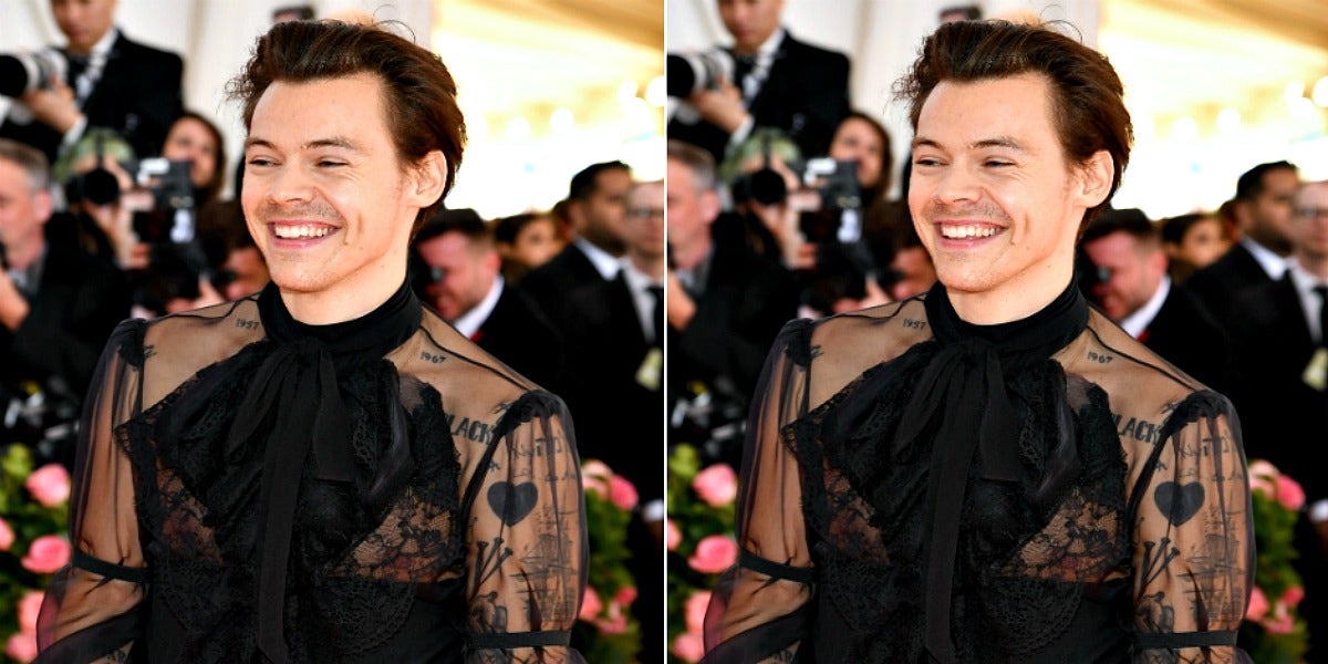 Harry Styles wears a lacy black top, his tattoos showing through