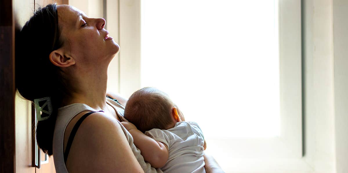 woman holding baby with back against wall