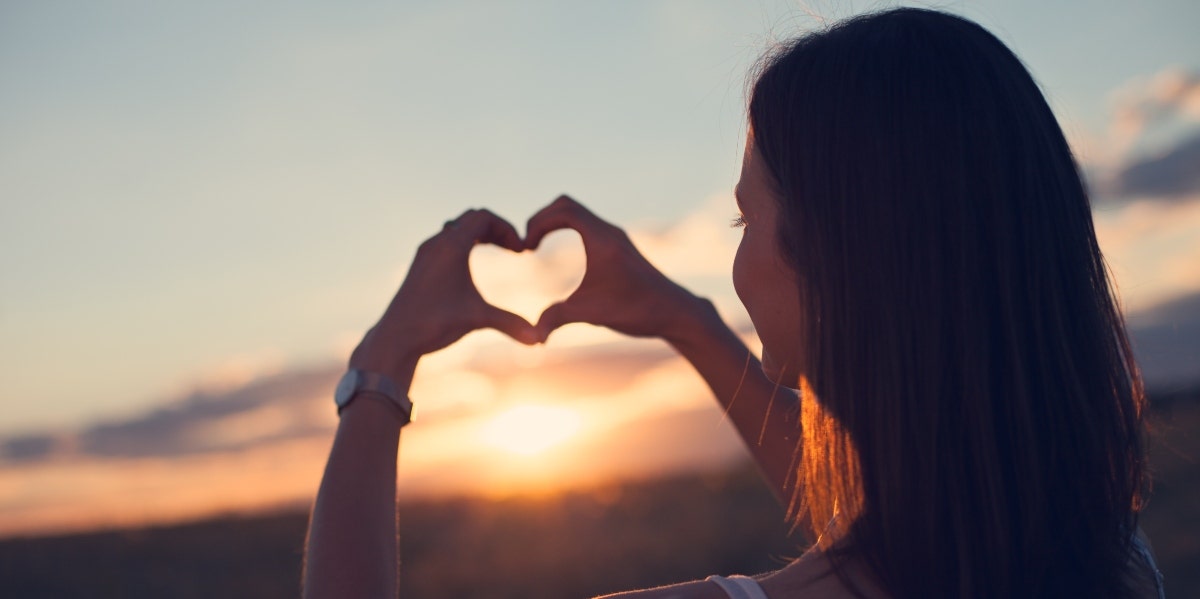 heart chakra woman making a heart in the sunset