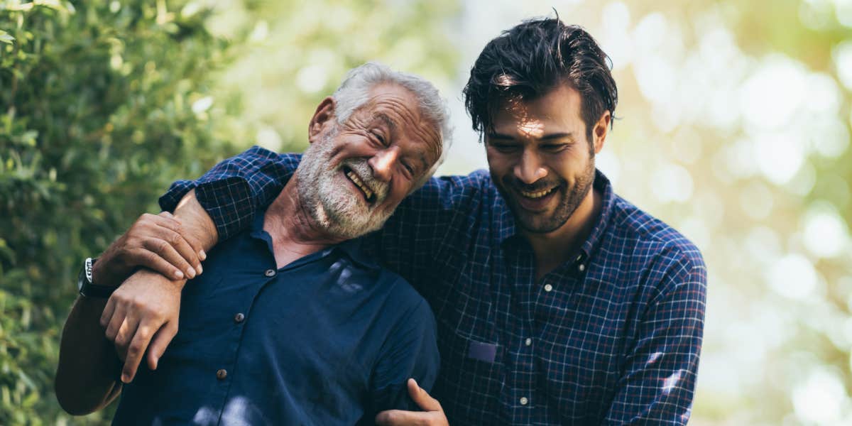 Elderly father with adult son, walking through a grove, arm around the other affectionately 