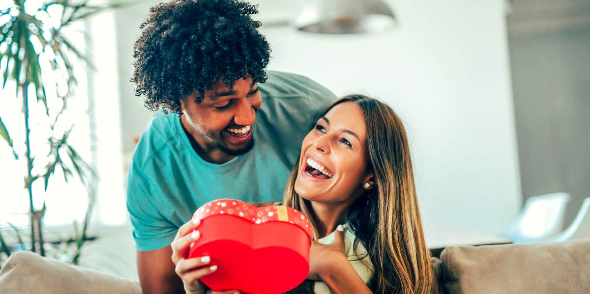 The Real History Of Why We Celebrate Valentine's Day couple celebrating Valentine's Day with a gift of chocolates in a heart-shaped box