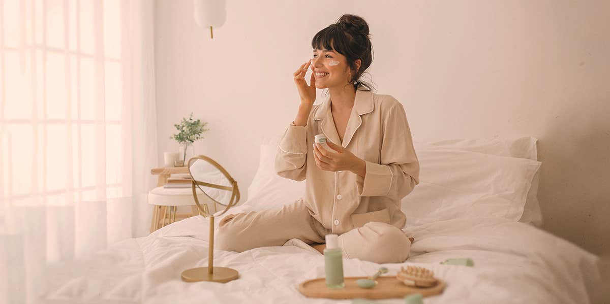 woman on bed putting lotion on face