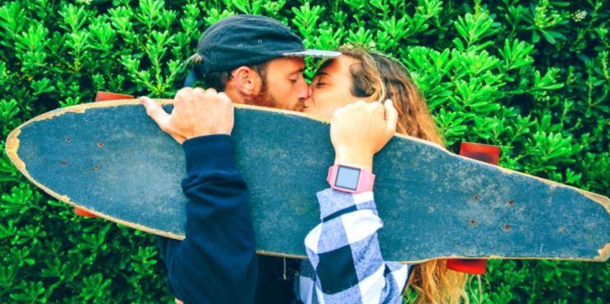 man and woman kissing and holding up skateboard