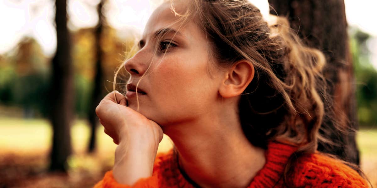 young woman in profile, chin in hand, thoughtful in an orange sweater