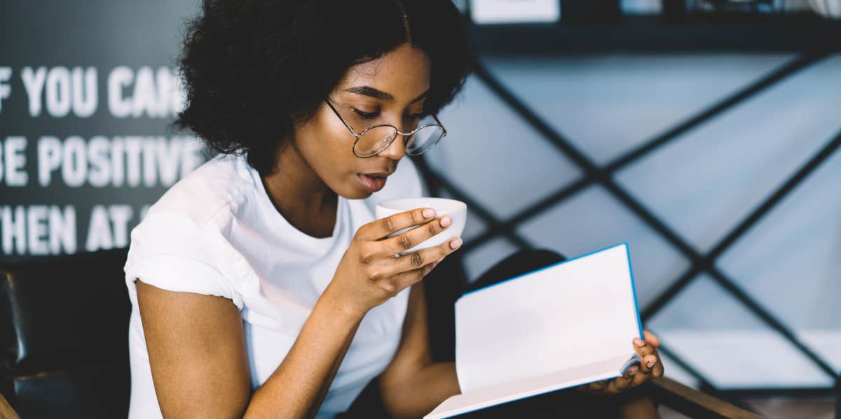 woman reading book while drinking coffee