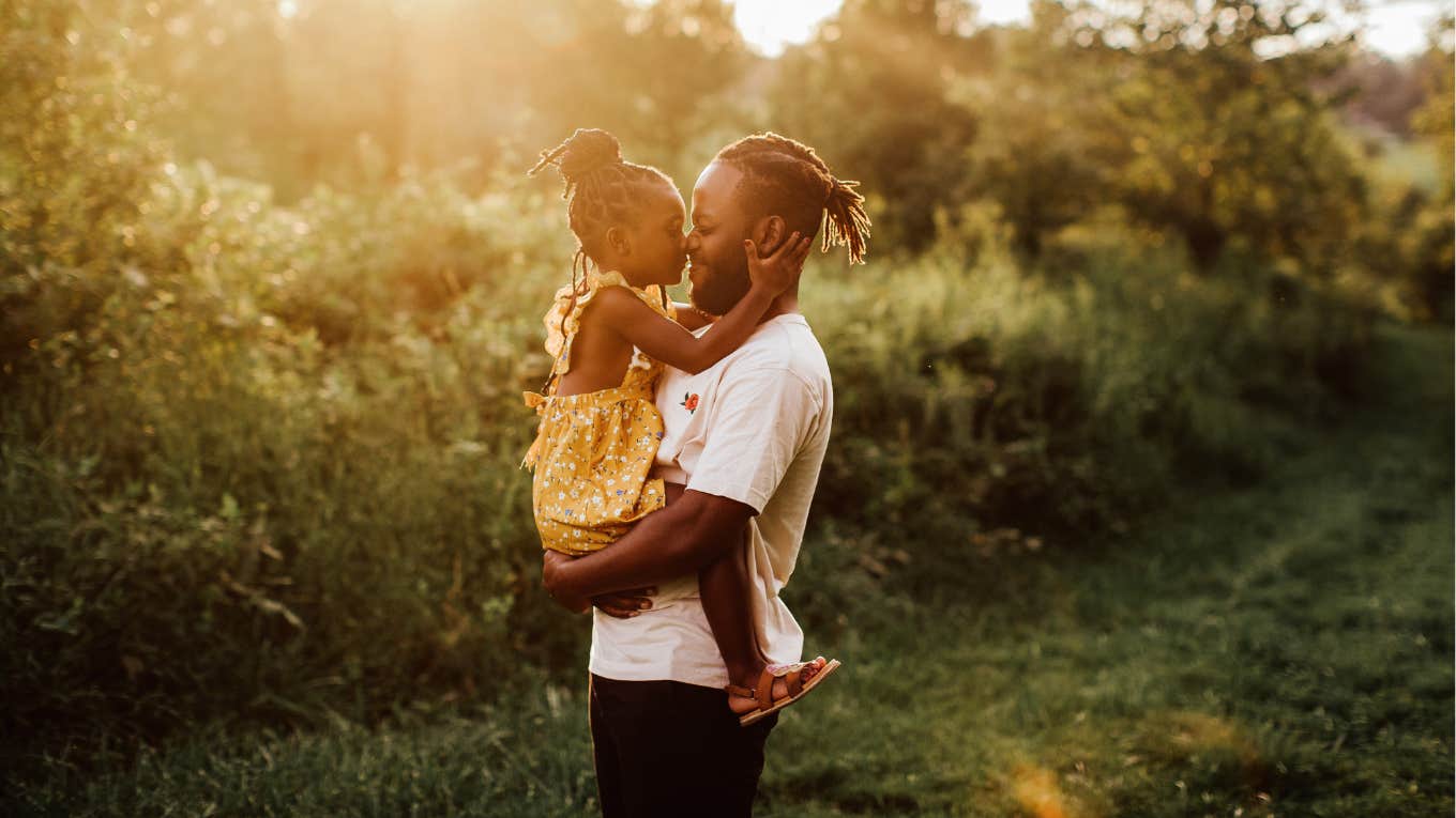 father holding young daughter in a sunlit field