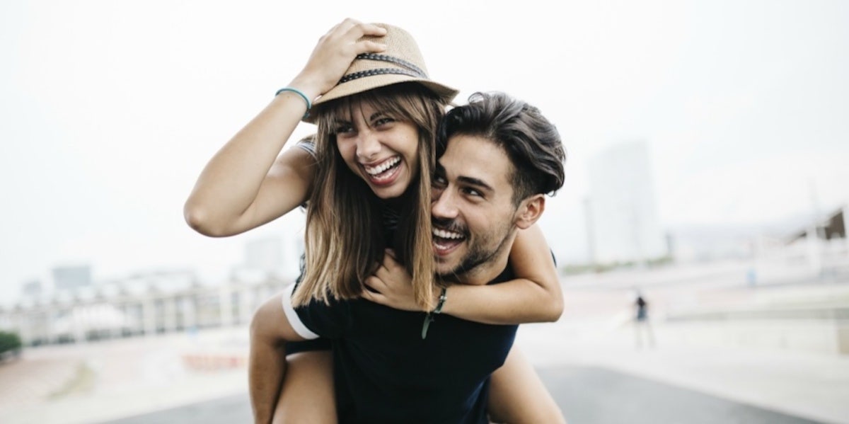 woman with hat smiling getting piggyback ride from man