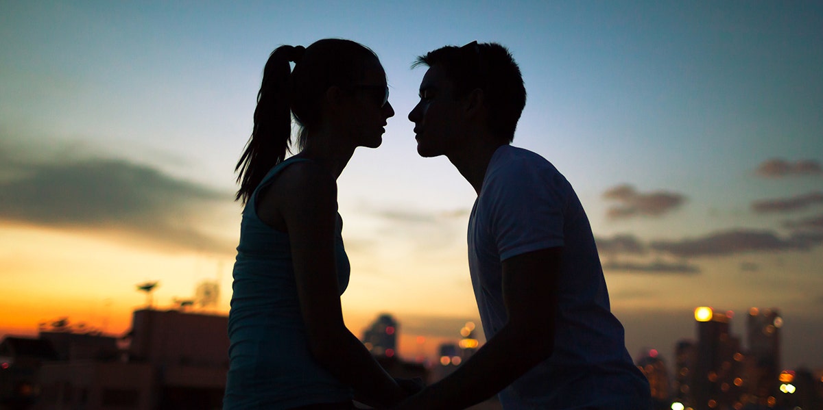 man and woman in shadow against sunset about to kiss