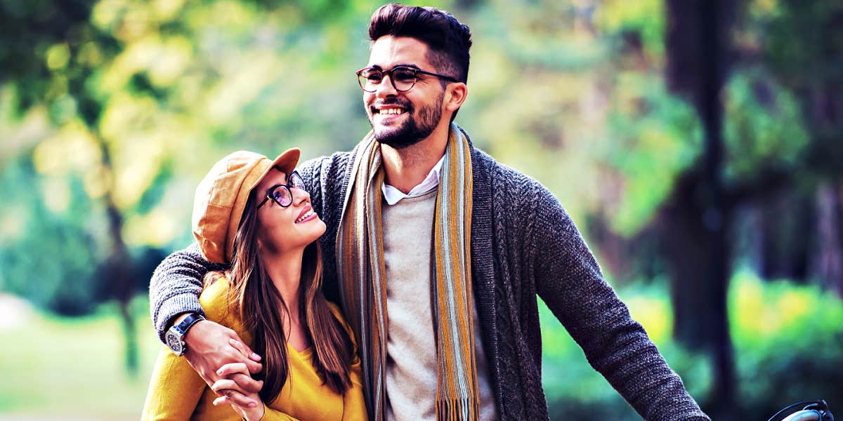 young couple with black hair and glasses walking through a woodsy park