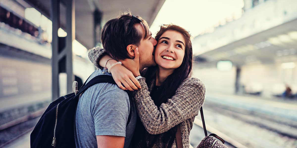 man kissing a woman on a train platform while she laughs 