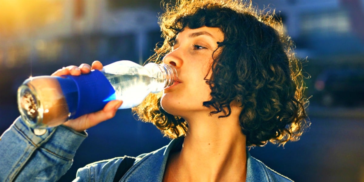 How Much Water You Should Be Drinking Every Single Day woman drinking from a bottle of water