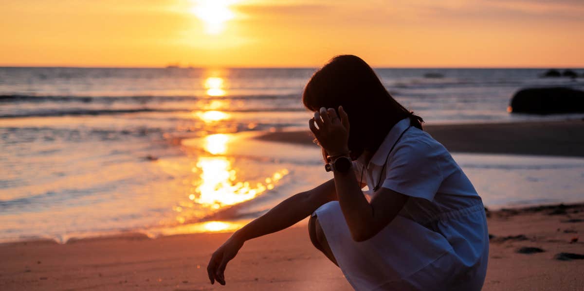grieving woman sitting on the beach at sunset