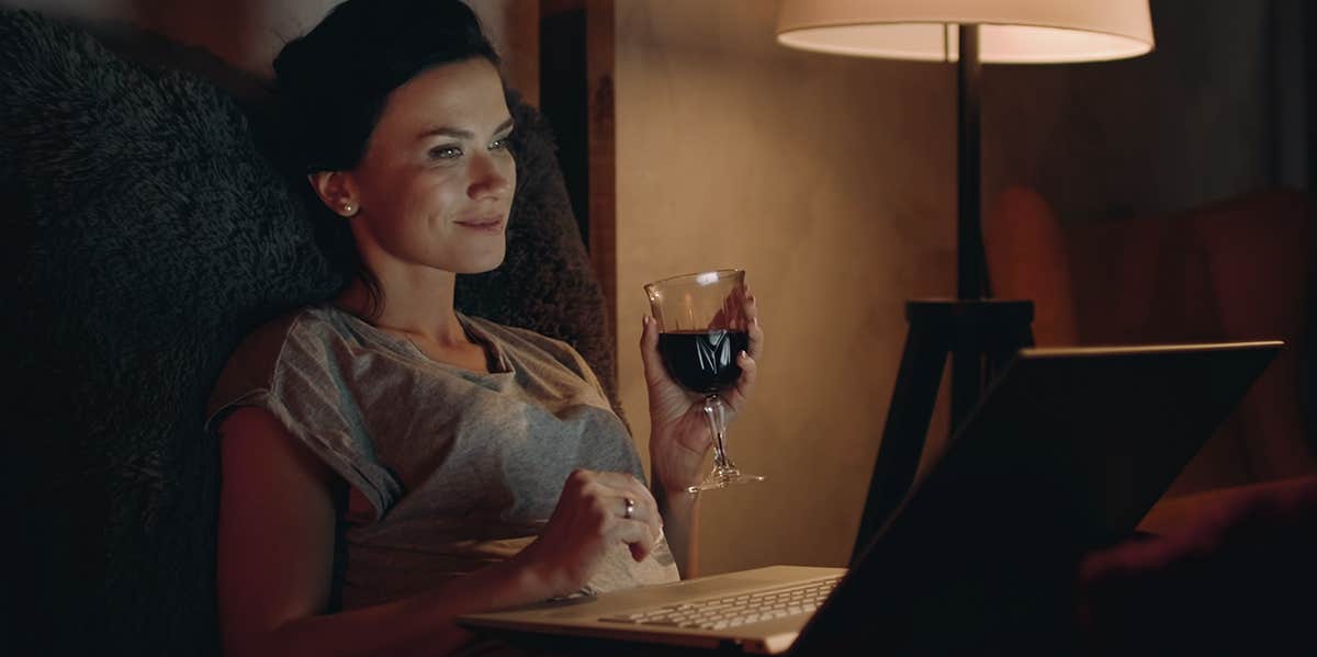 woman laying in bed on laptop drinking wine
