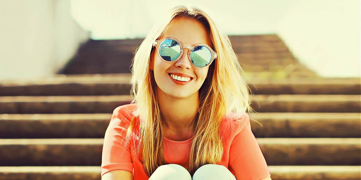 blonde woman smiles confidently at camera, sitting on outdoor steps