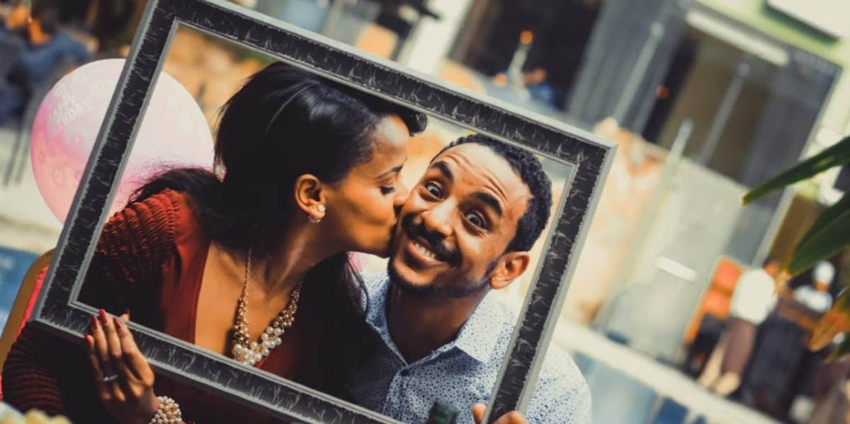 woman kissing excited man's cheek inside a picture frame