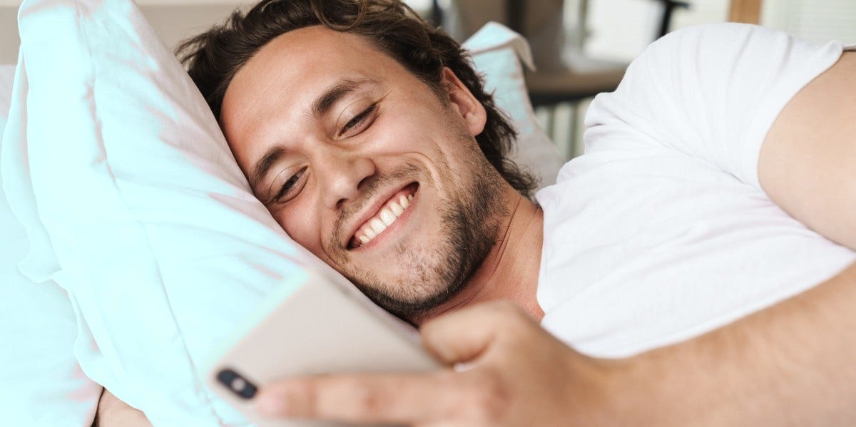 man laying in bed smiling at his phone
