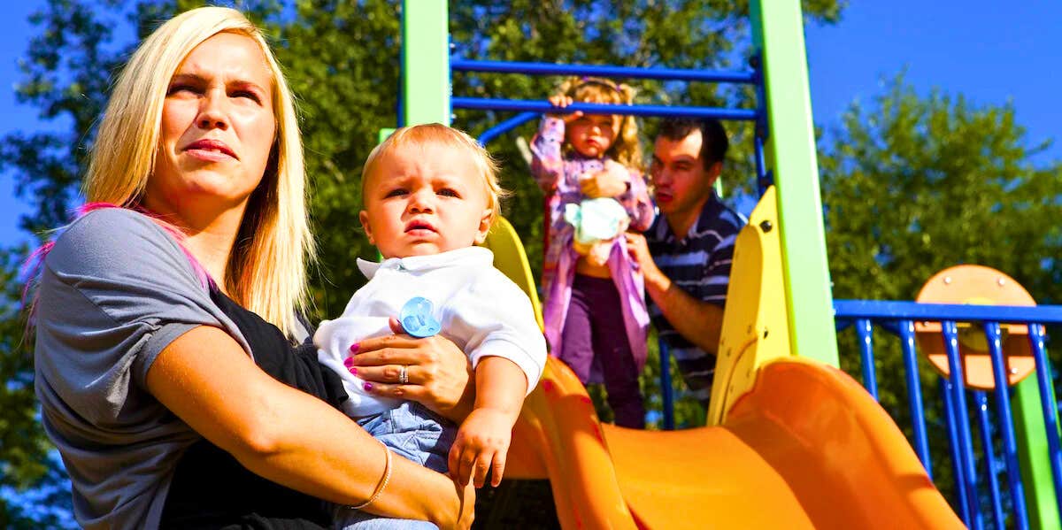 exes who hate each other playing with their children on a playground