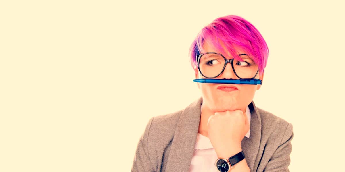 Pink haired woman distracts herself by balancing pencil on upper lip