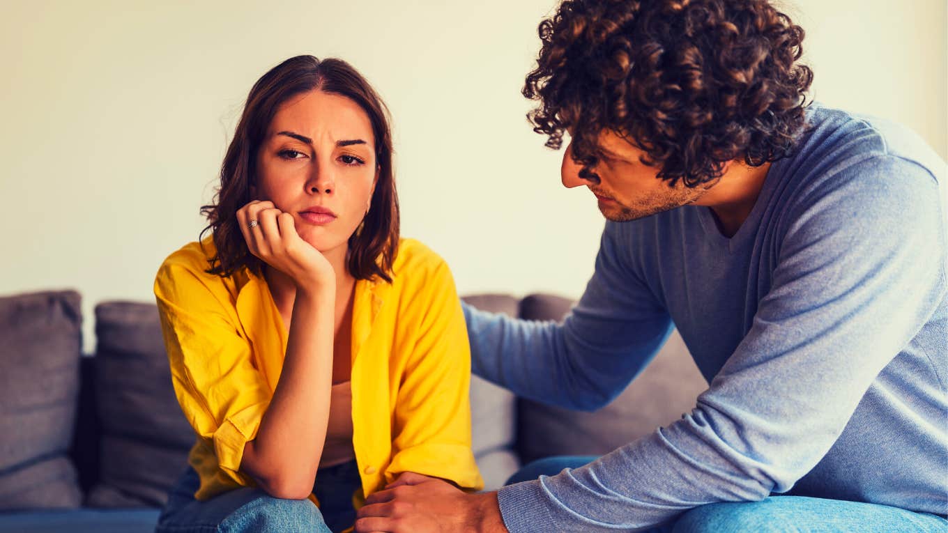 man and woman sitting on the couch, he is trying to get her to talk to him