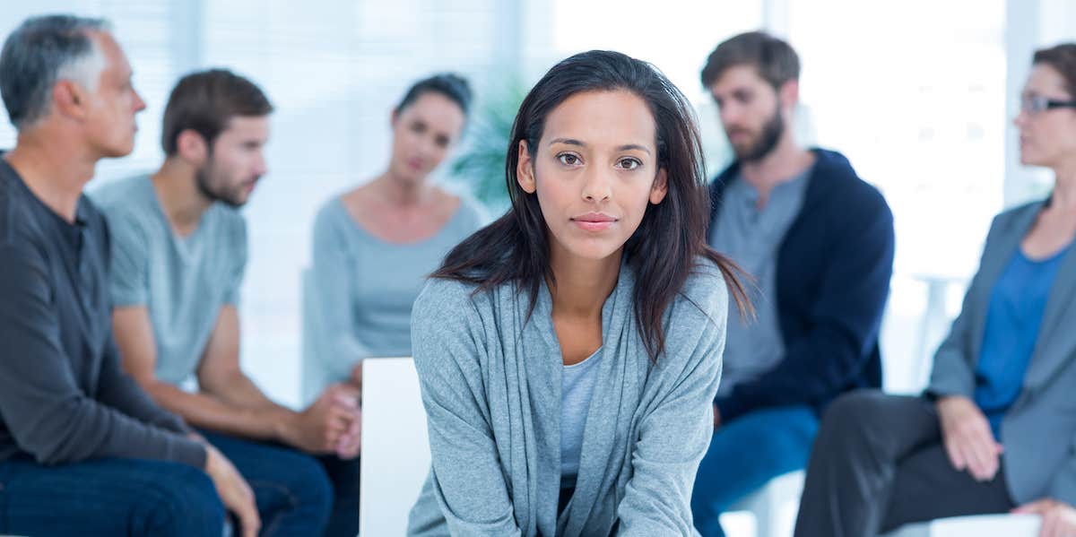 A group of people sit in the back ground as a woman looks invitingly at the camera