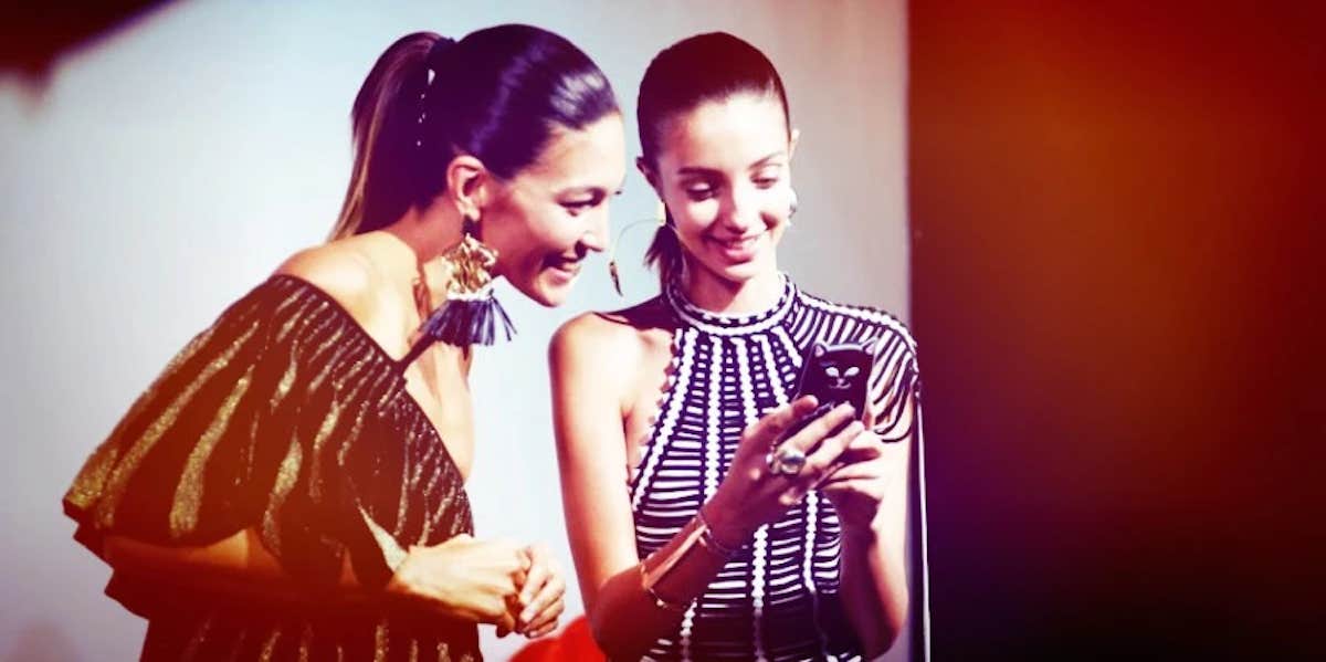 two women smiling while excitedly looking at the screen of the phone one of the women is holding