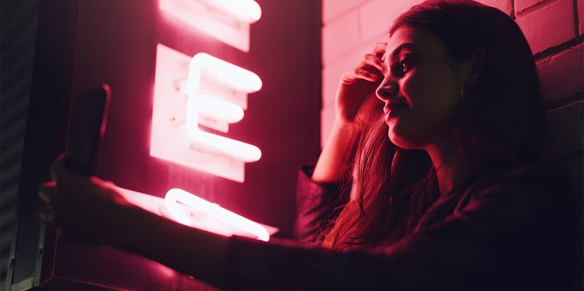 woman taking selfie near pink neon light