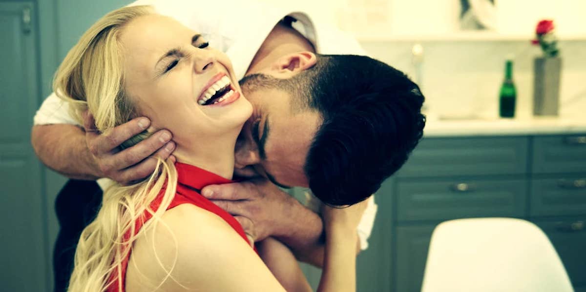 a seated woman laughs in pleasure as a man kisses her neck from behind her