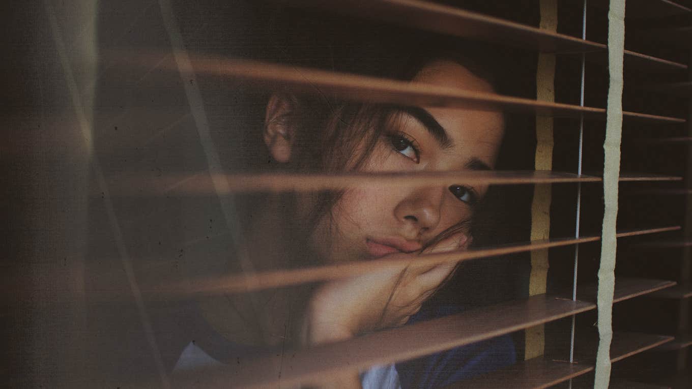 Woman looking sadly out her blinds 
