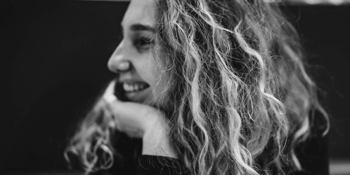 Black and white image of a woman in her 30s smiling away from camera, long curly light brown hair