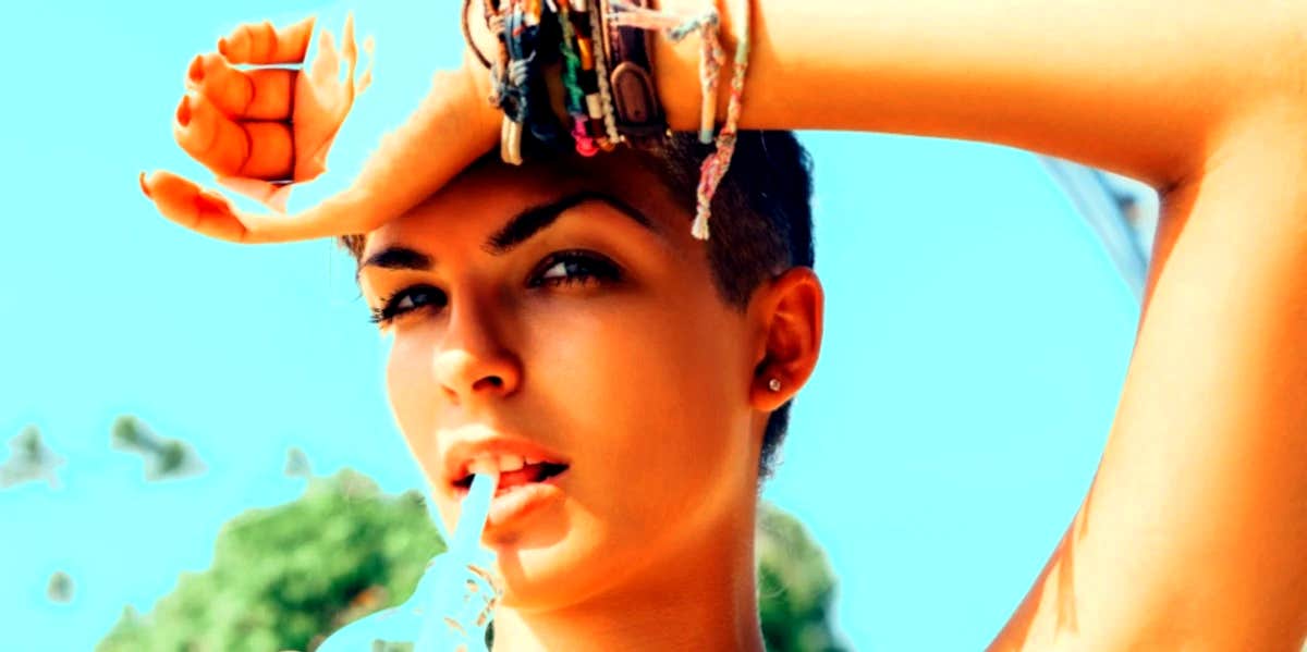 woman with one arm over her head drinking from a straw