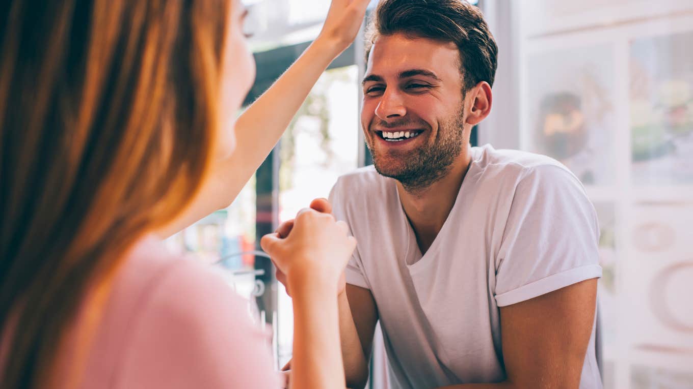 Joyful laughing romantic man in love holding hand of partner during flirting and showing care with tenderness while girlfriend touching hair